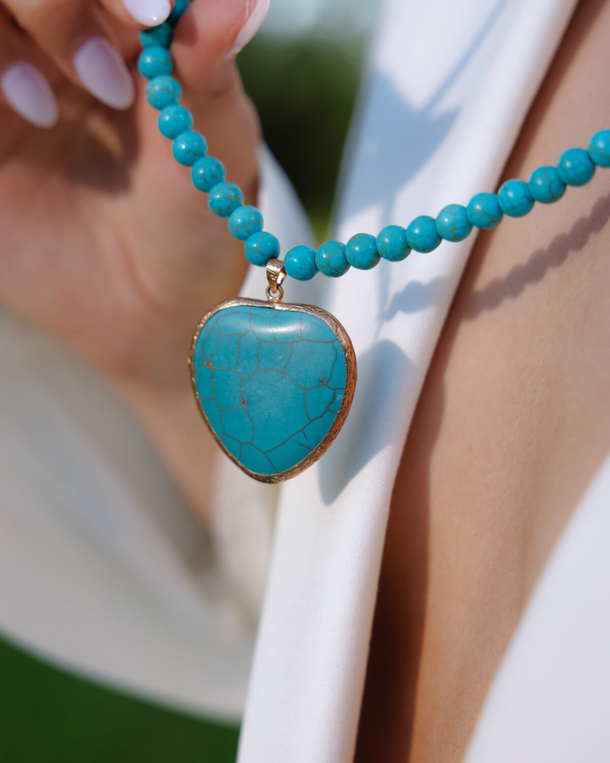 Turquoise heart pendant worn over a white shirt