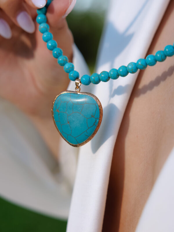Turquoise heart pendant worn over a white shirt
