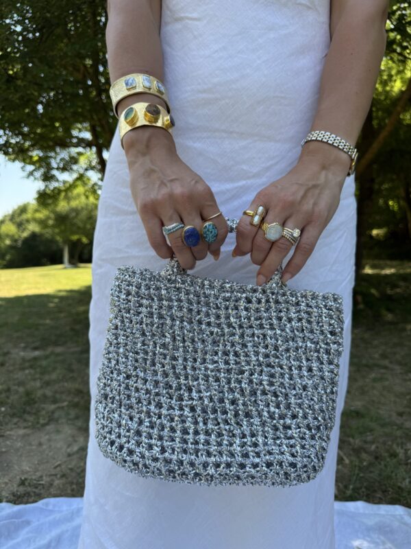 Hands holding a handmade raffia bag, wearing gold rings and cuffs